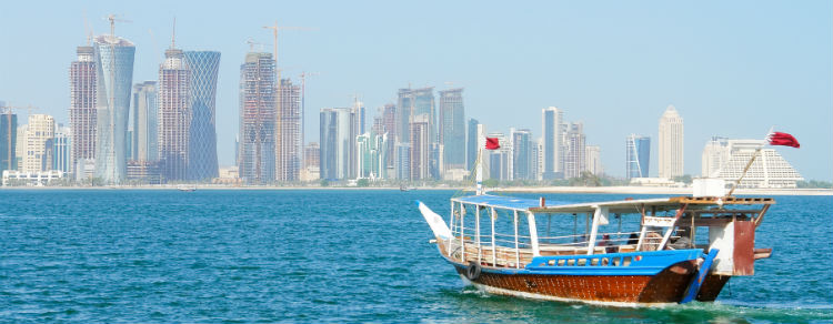 The skyline of Doha seen in the background over water with a water vessel in the foreground.