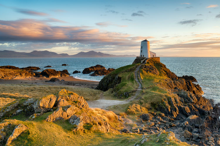 A lighthouse against a rocky coastline in Wales. The photo is taken from the mainland looking out