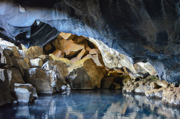 A rocky cave with a pool at the bottom. 