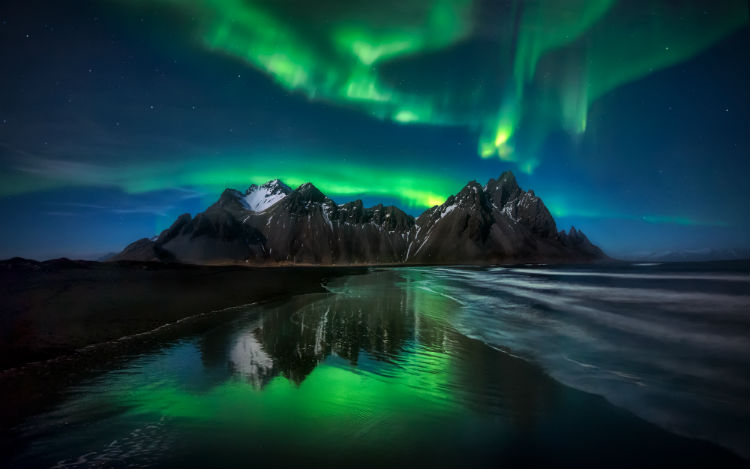 Green northern lights above some rocky cliffs in Iceland. 