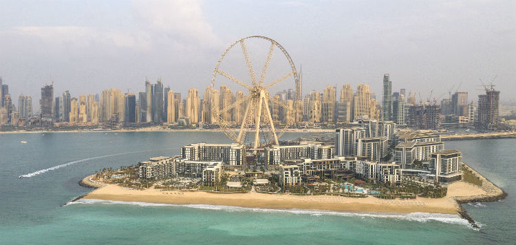 An image of Caesars Bluewaters Resorts from the water. you can see the skyline of Dubai in the background