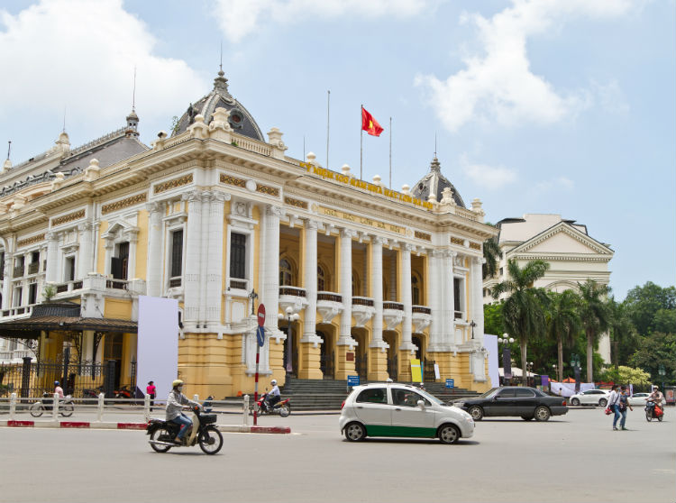 Hanoi Opera House during the day with cars driving in front of it. 