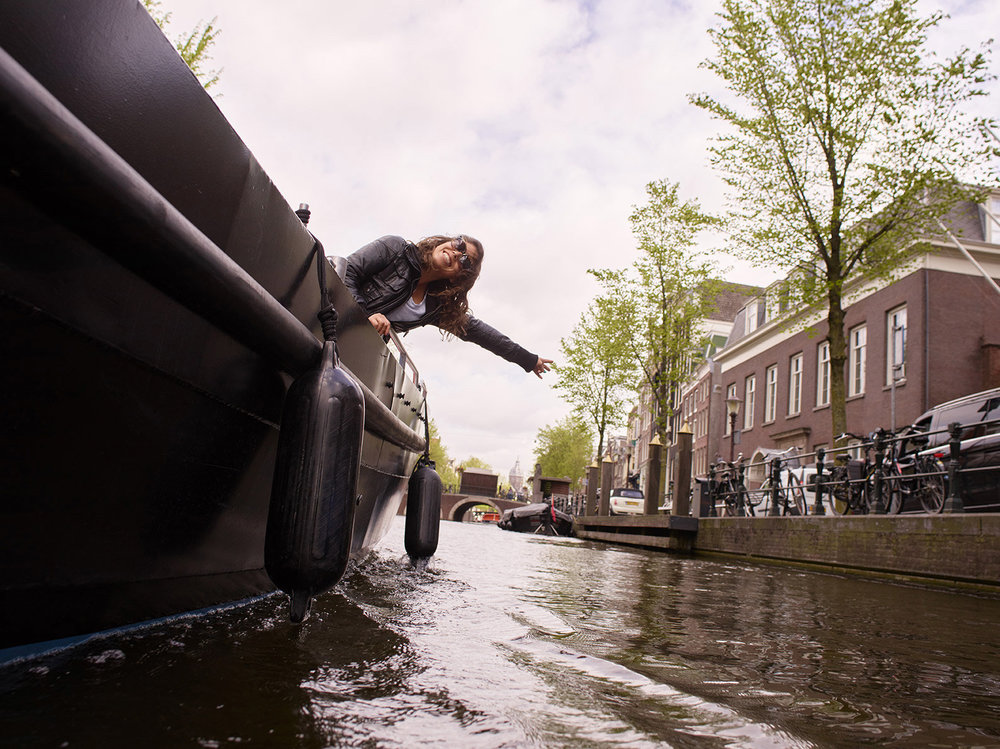 A woman on a river cruise in Amsterdam, she is waving from the side of the boat. 