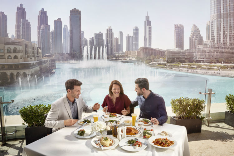 Three adults enjoying a meal with the Dubai Marina in the background. 