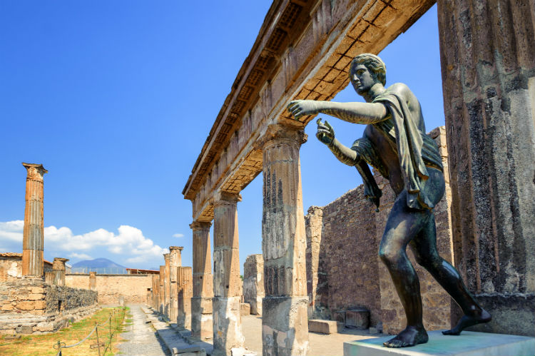 A statue on the right hands side leaning onto a walking path in the ruined city of Pompeii