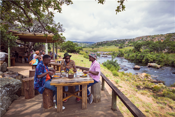 Three men enjoying a dinner with a river in the background. 