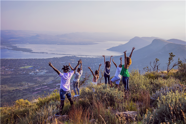 A group of people with their hands in the air up a mountain looking down on a city, 