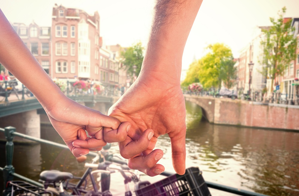 A picture of a couple holding pinkies in Amsterdam. They are in front of the canal