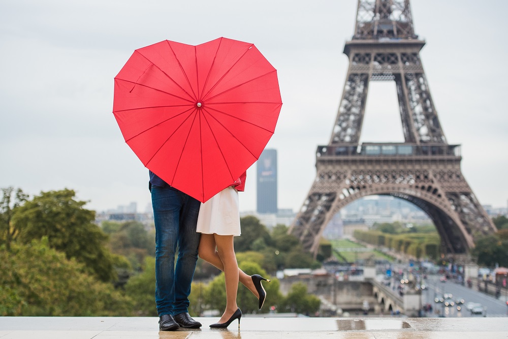 A picture of a couple in front of the Eiffel Tower. They are hidden by a heart-shaped umbrella