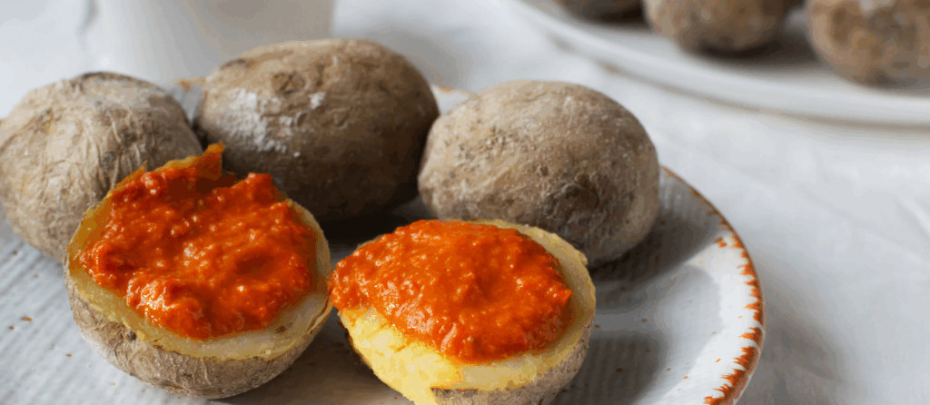 Potatoes on a white plate with red sauce on a white tablecloth. A traditional Canarian dish is papas arrugadas. Vegetables are boiled in water with a lot of salt.