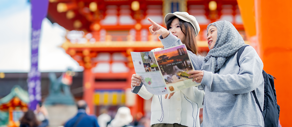 Visitors learning about history of fushimi inari shrine in travel book while walking through senbon torii path in Kyoto Japan